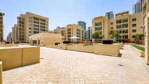 A residential building complex with multiple apartment buildings, a paved courtyard, and some greenery. - Quiet 2BR Haven Steps from The Greens Lakes and Emirates Golf Club,Al Dhafrah 2 (Dubai)