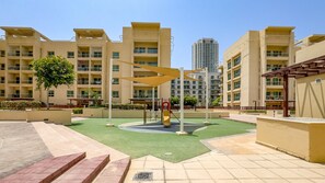 A residential building with multiple balconies, a playground with a slide, and a green lawn area. - Quiet 2BR Haven Steps from The Greens Lakes and Emirates Golf Club,Al Dhafrah 2 (Dubai)