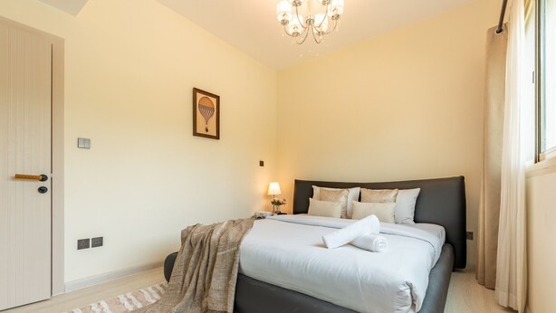 A bedroom with a bed, bedside table, lamp, and a framed picture on the wall. - Quiet 2BR Haven Steps from The Greens Lakes and Emirates Golf Club,Al Dhafrah 2 (Dubai)