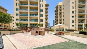 Un edificio residencial con varios balcones, un patio empedrado con mesas de picnic y una pequeña construcción de ladrillo.