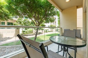 A balcony with a glass table and chairs, overlooking a courtyard with trees and a building in the background. - Quiet 2BR Haven Steps from The Greens Lakes and Emirates Golf Club,Al Dhafrah 2 (Dubai)