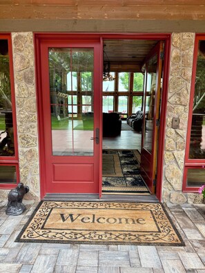 A red door with a welcome mat, stone walls, and a view of the outdoor area.