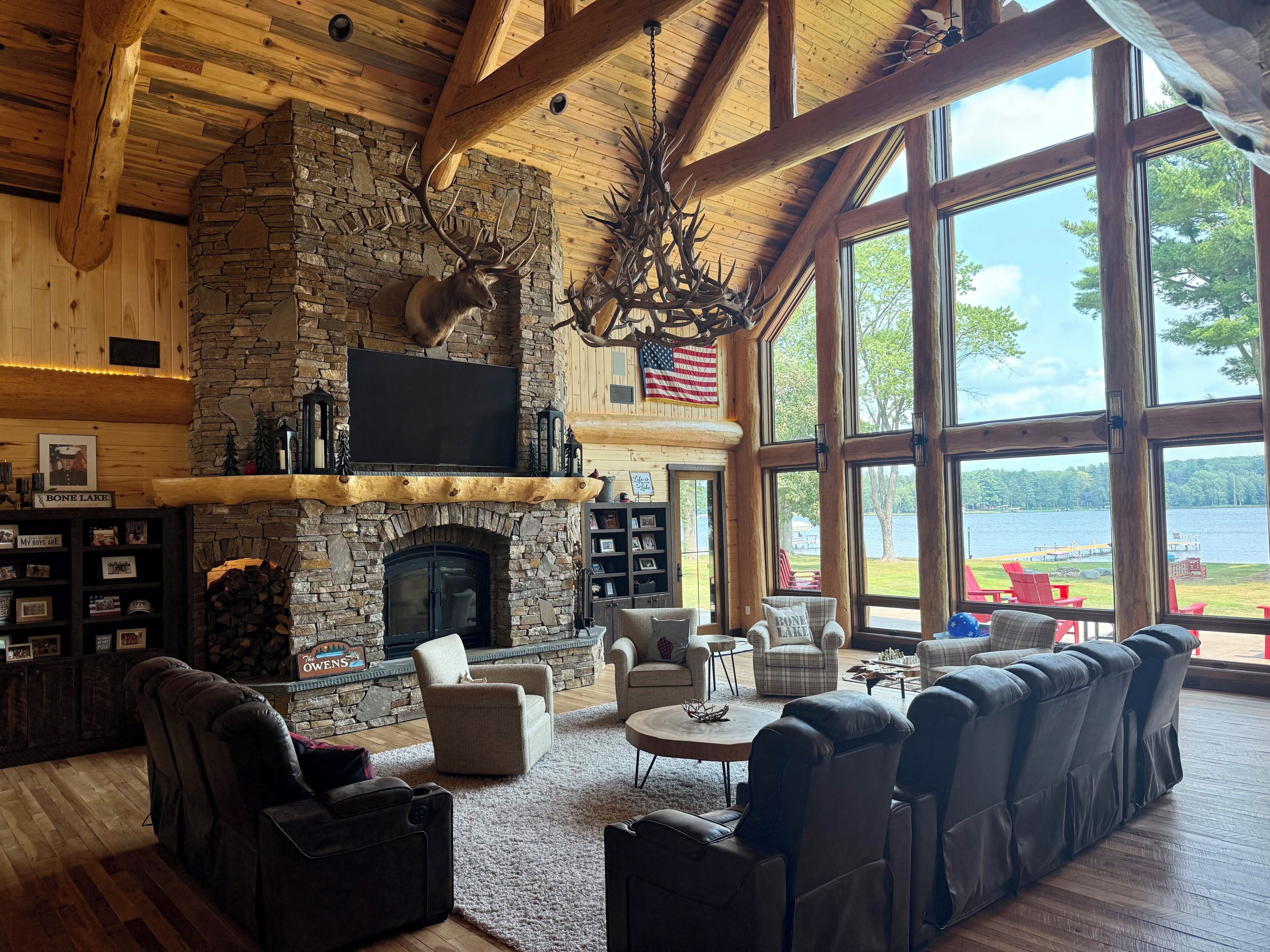 A spacious living room with a stone fireplace, leather sofas, and a large window overlooking a lake.