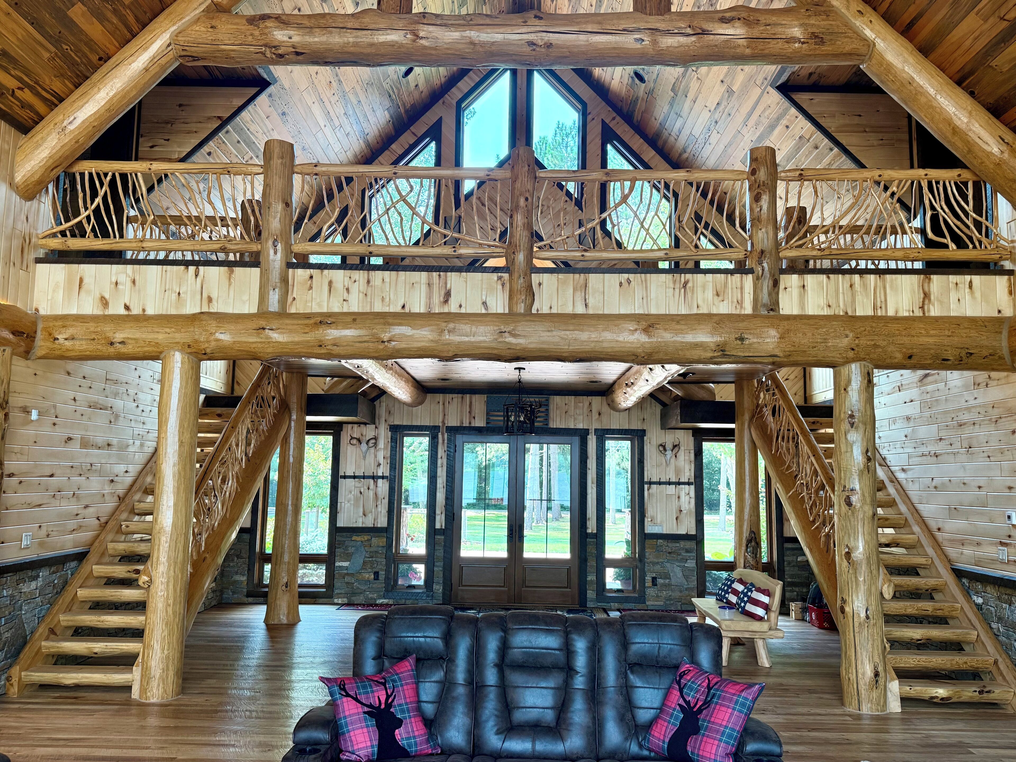 A spacious interior with a high ceiling, wooden beams, a fireplace, a leather sofa, and a staircase.