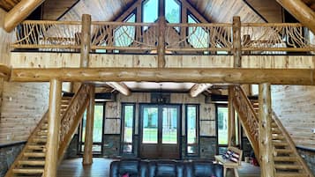 A spacious interior with a high ceiling, wooden beams, a fireplace, a leather sofa, and a staircase.