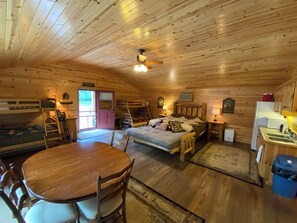 A cabin with a bunk bed, a dining table with chairs, a kitchen area, and a ceiling fan. - Spacious 5-bedroom lodge on Bone Lake with 2 guest cabins, pickleball and sauna. (Milltown)