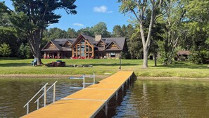 A lodge with a dock extending into a lake, surrounded by trees and a grassy area with outdoor seating.