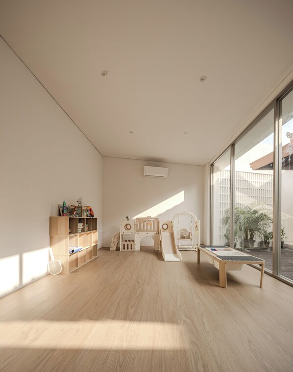 A spacious room with a large window, a play area with a slide, and a wooden bookshelf.