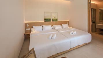 A hotel room with a large bed, a bedside table, a chair, and a small table with a bottle.