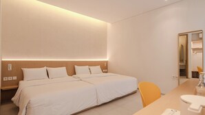 A modern hotel room with a large bed, bedside tables, a desk with a chair, and a hanging light fixture.