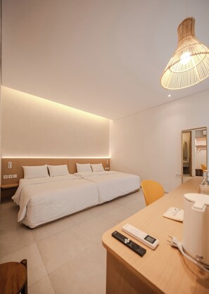 A modern hotel room with a large bed, bedside tables, a desk with a chair, and a hanging light fixture.