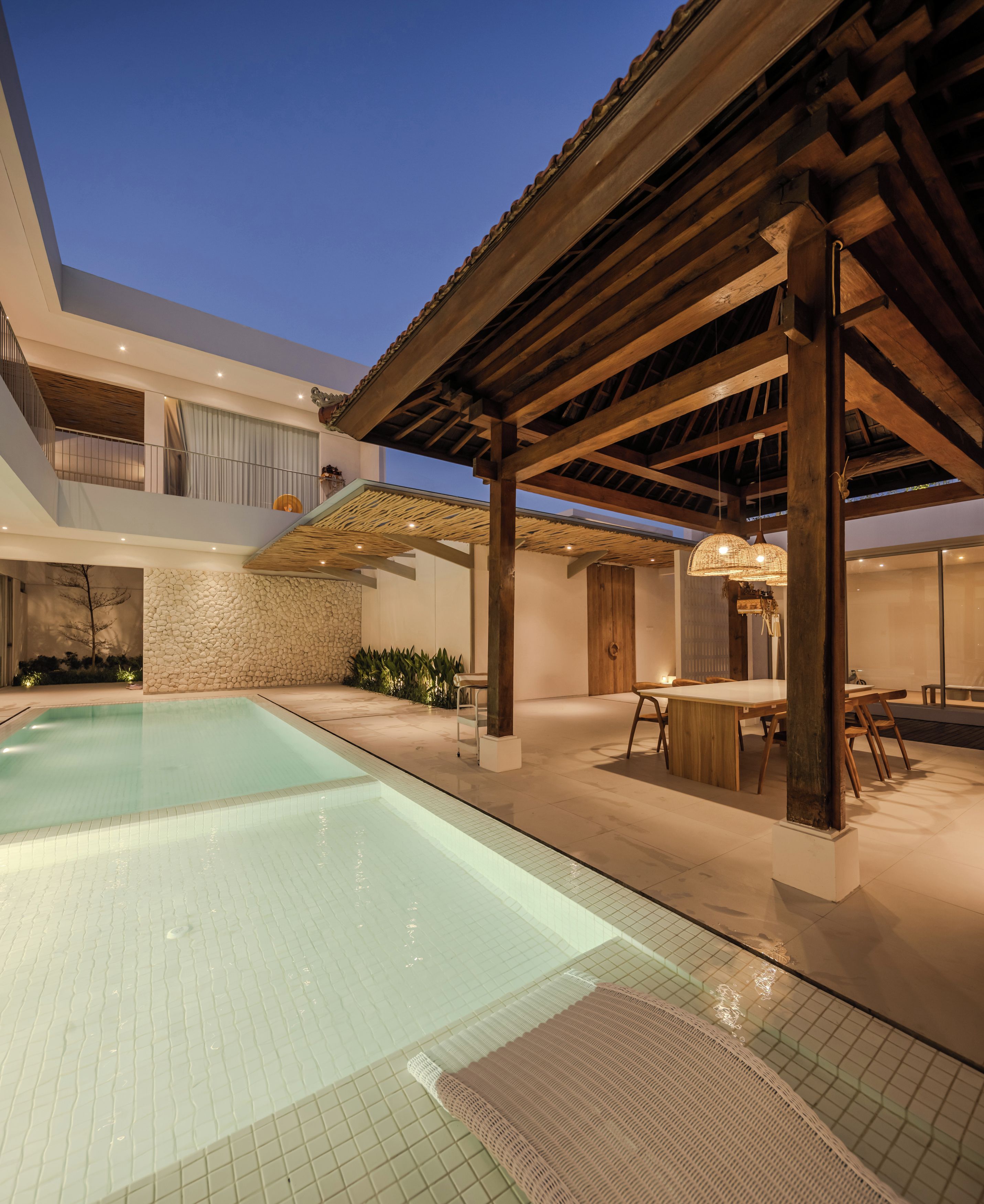 A modern outdoor pool area with a pergola, stone wall, and a dining area with a table and chairs.