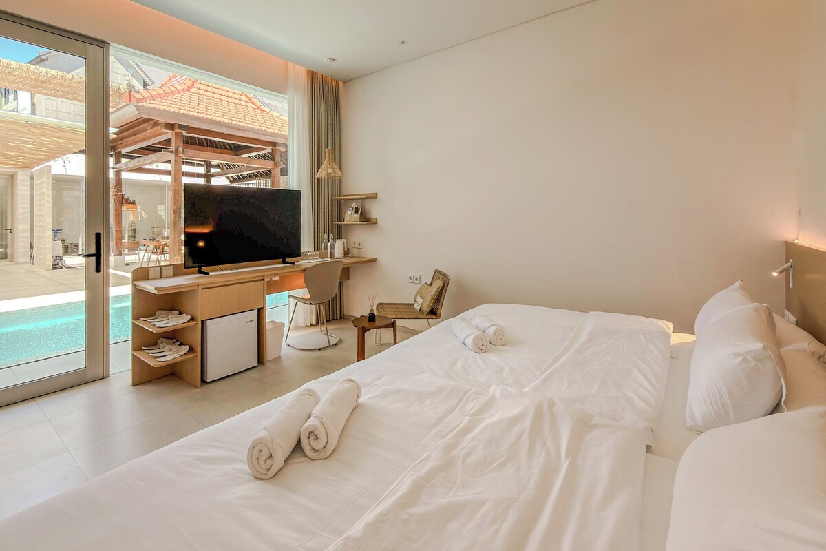 Habitación de hotel con cama, escritorio con computadora, televisor y vista a una piscina y zona exterior.