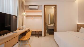 A hotel room with a bed, a desk, a chair, a TV, a mirror, and a bathroom visible through an open door.