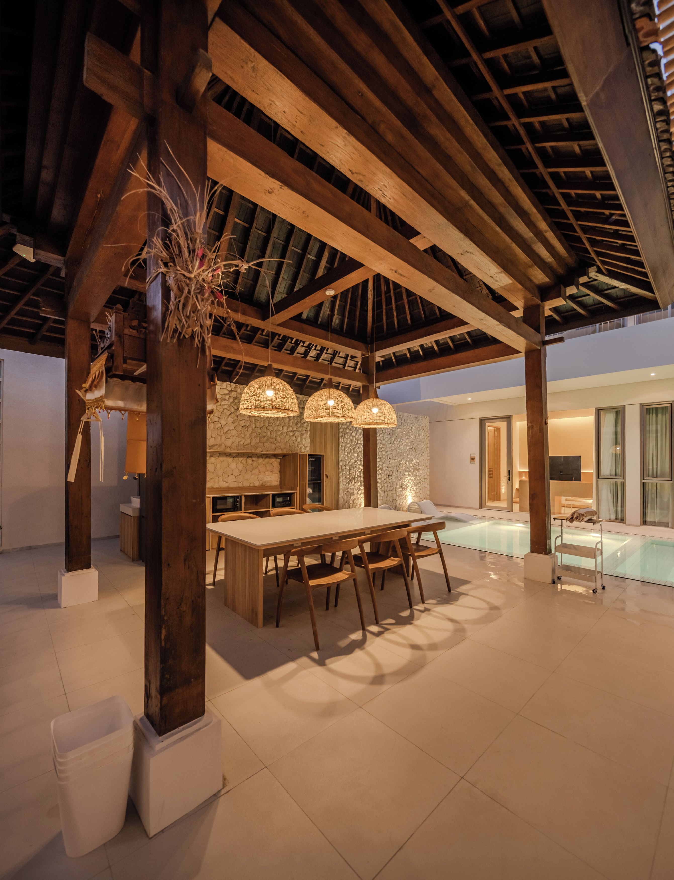 A spacious indoor area with a large wooden table and chairs, a stone wall, and a pool area.