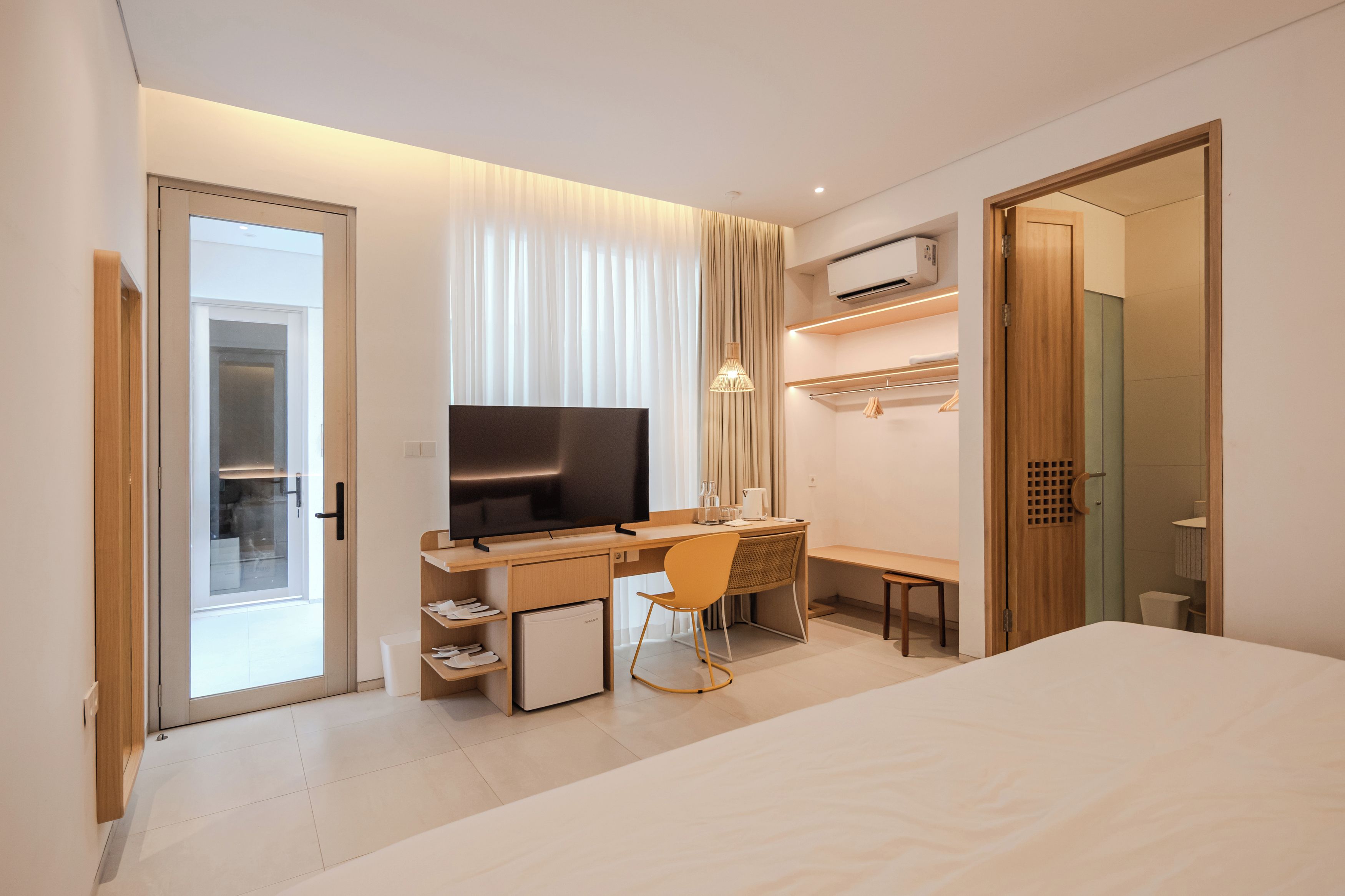 Ein modernes Hotelzimmer mit einem Bett, einem Schreibtisch mit Stuhl, einem Fernseher und einem Kleiderschrank.