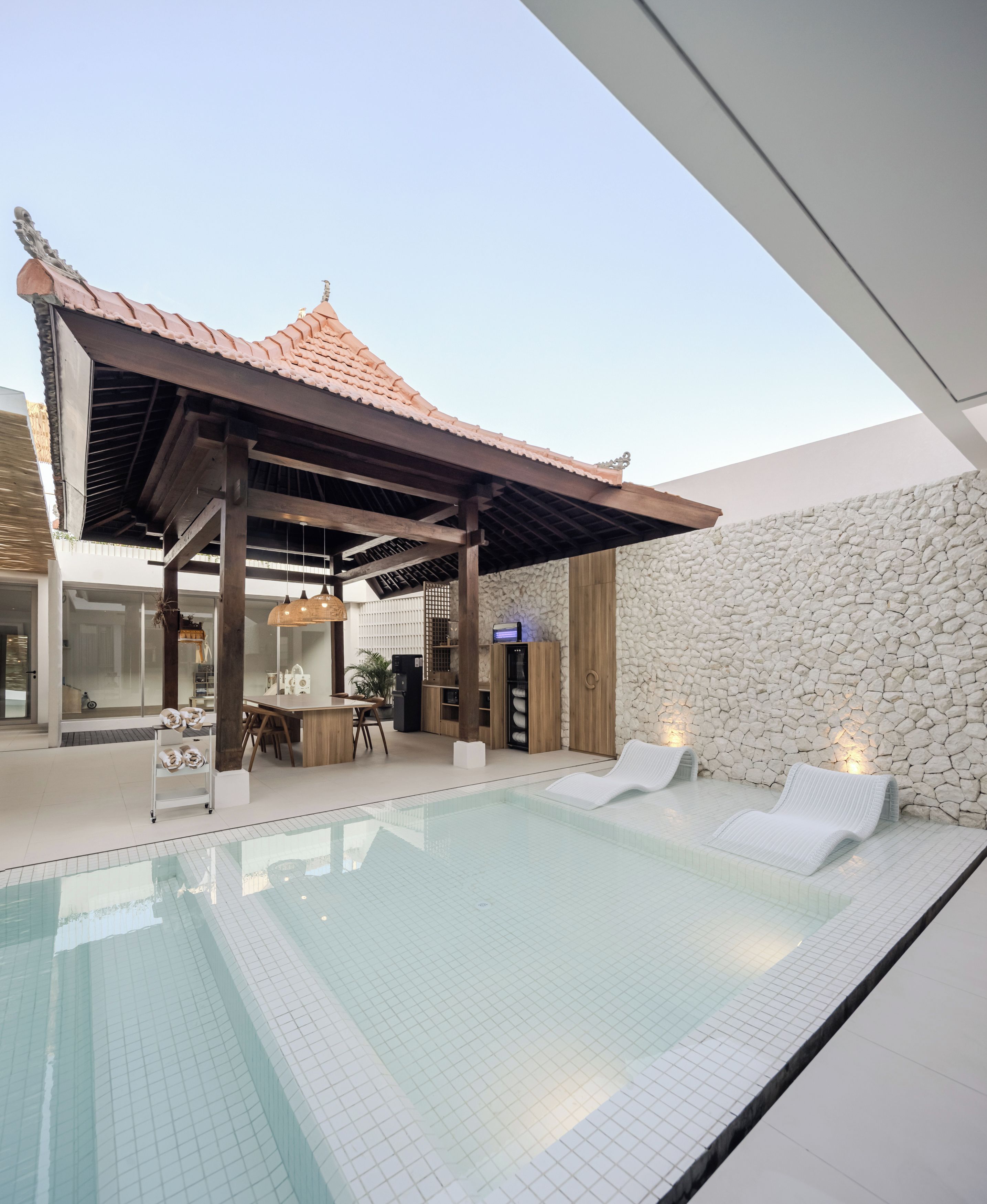 A modern outdoor pool area with a covered seating area and a stone wall.