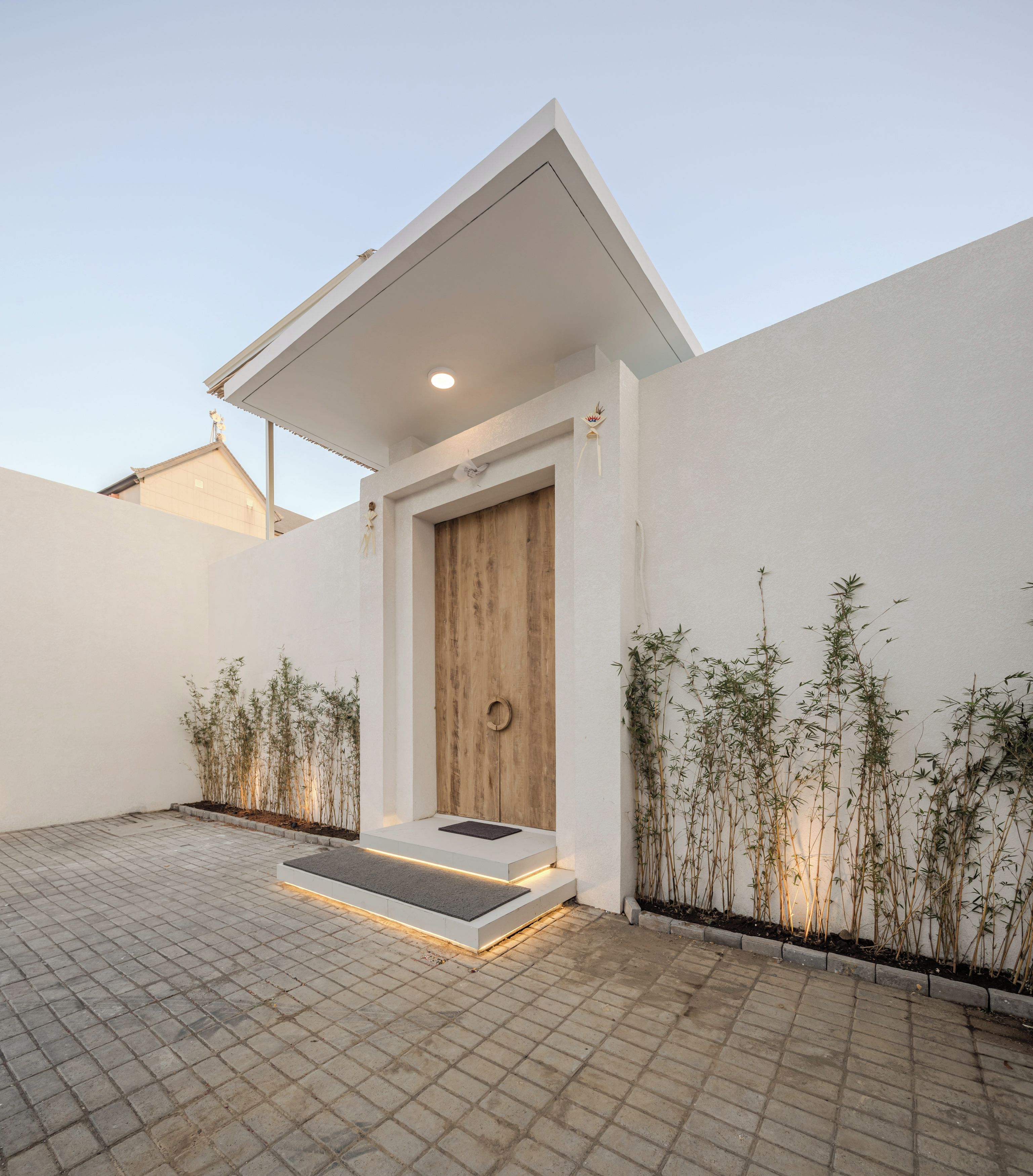 A modern house with a wooden door, white walls, and a tiled patio.