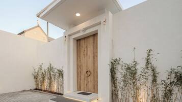 A modern house with a wooden door, white walls, and a tiled patio.