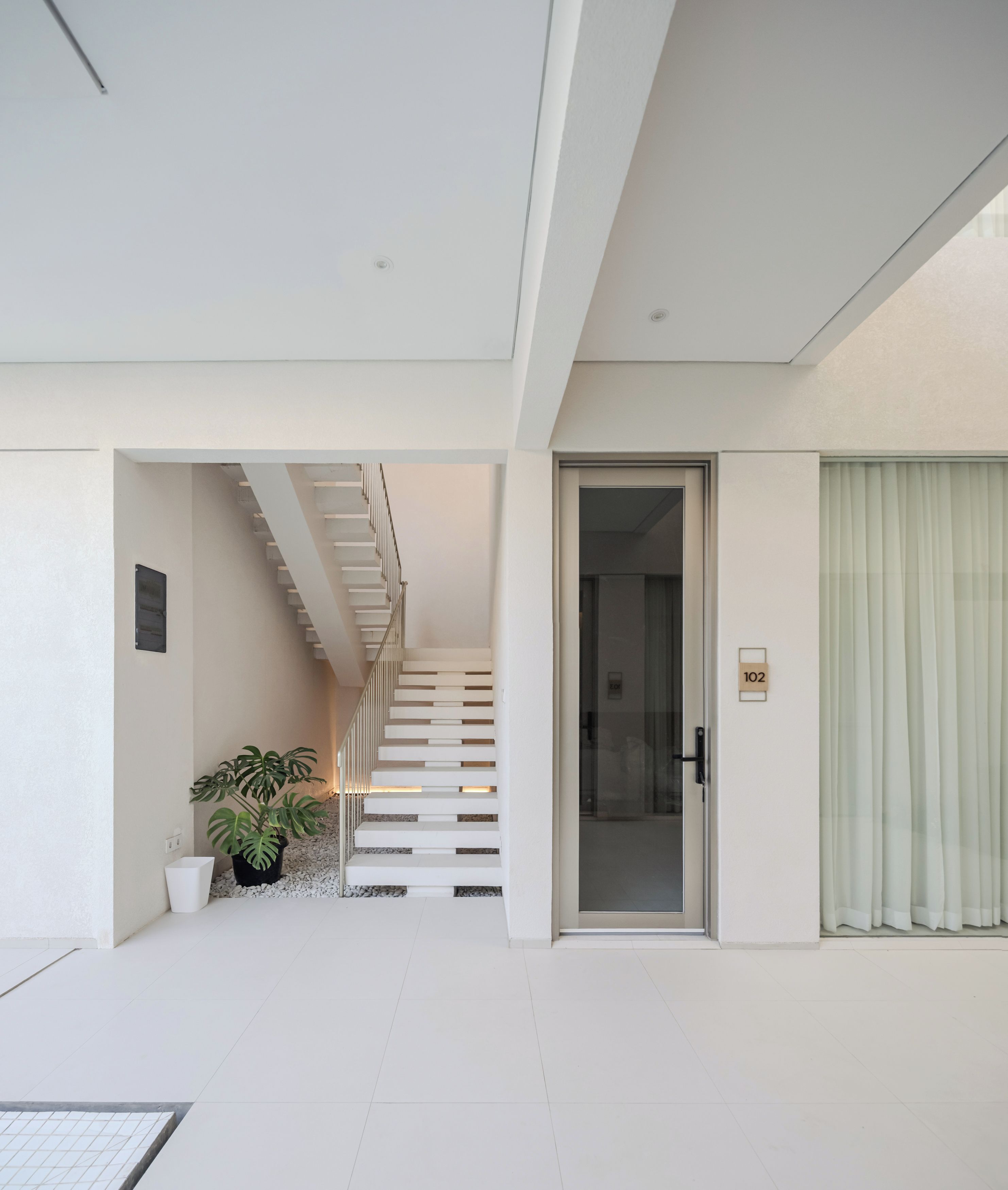 Een modern interieur met een trap naar een tweede verdieping, een glazen deur met een nummer en een potplant.
