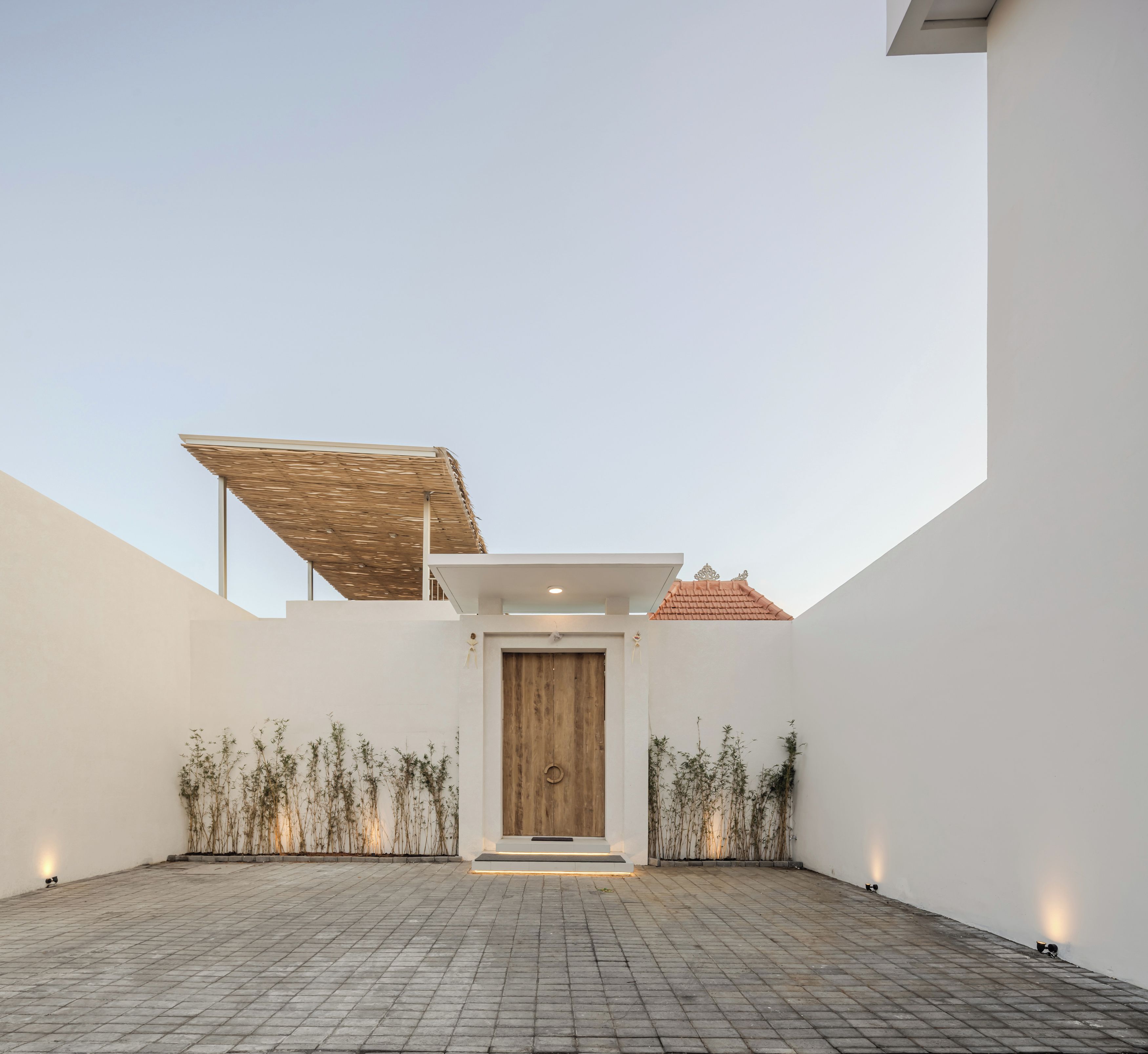 A modern building with a central wooden door, a brick-paved courtyard, and a sloped roof structure.