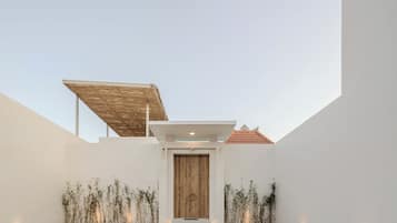A modern building with a central wooden door, a brick-paved courtyard, and a sloped roof structure.