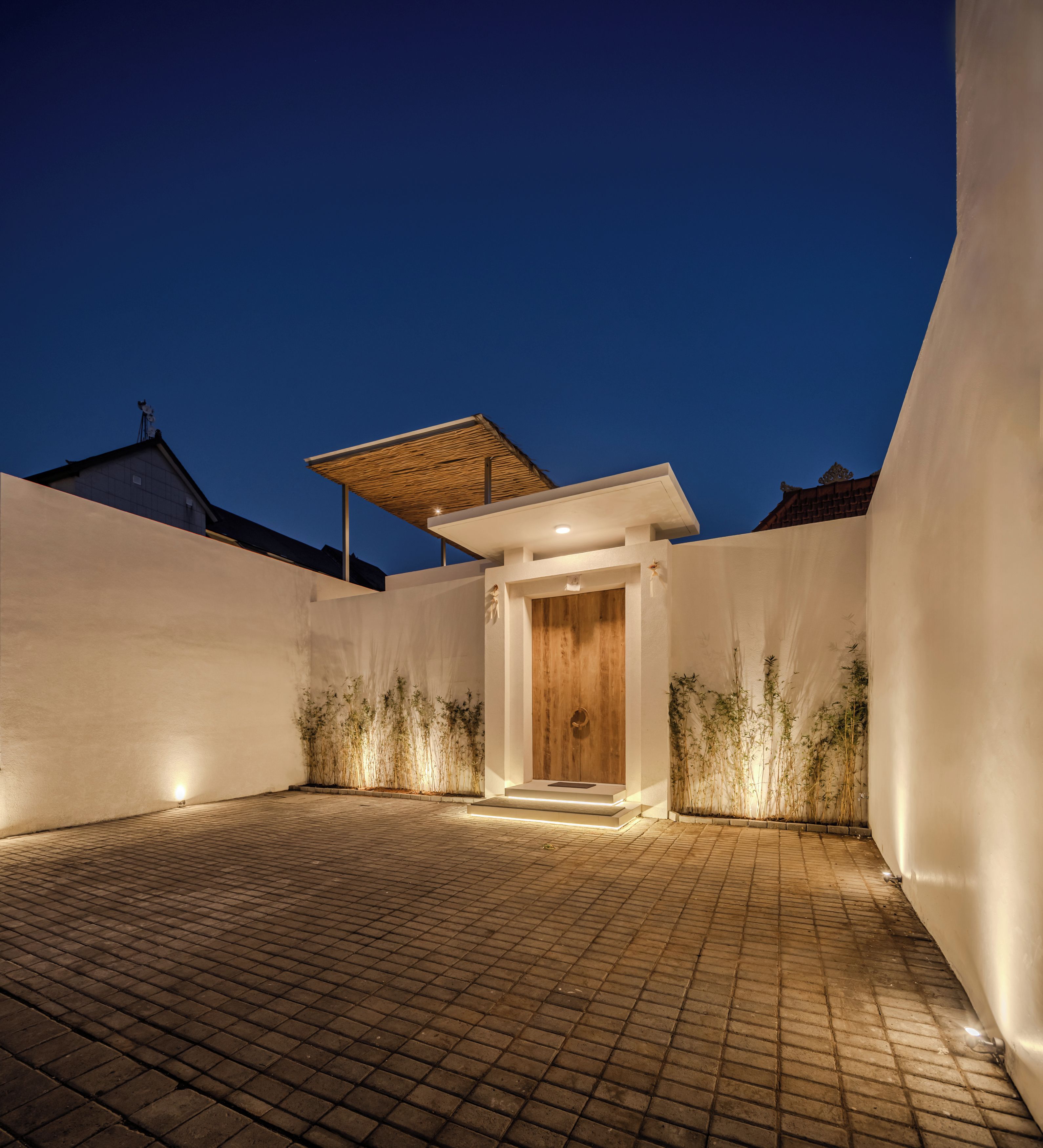 A modern building with a wooden door entrance, a brick-paved courtyard, and a covered area with a thatched roof.