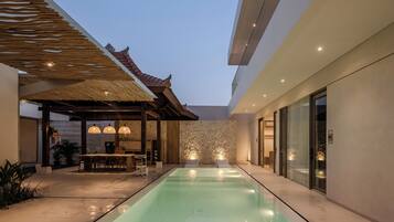 A modern pool area with a clear pool, a covered seating area, and a stone wall.