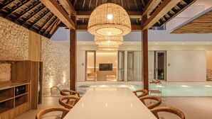 A spacious dining area with a long table and chairs, a hanging light fixture, and a stone wall.