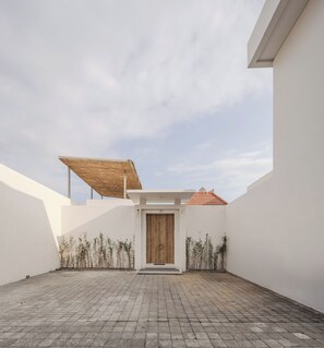 Un patio con puerta de madera, piso de baldosas y estructura de techo de paja.