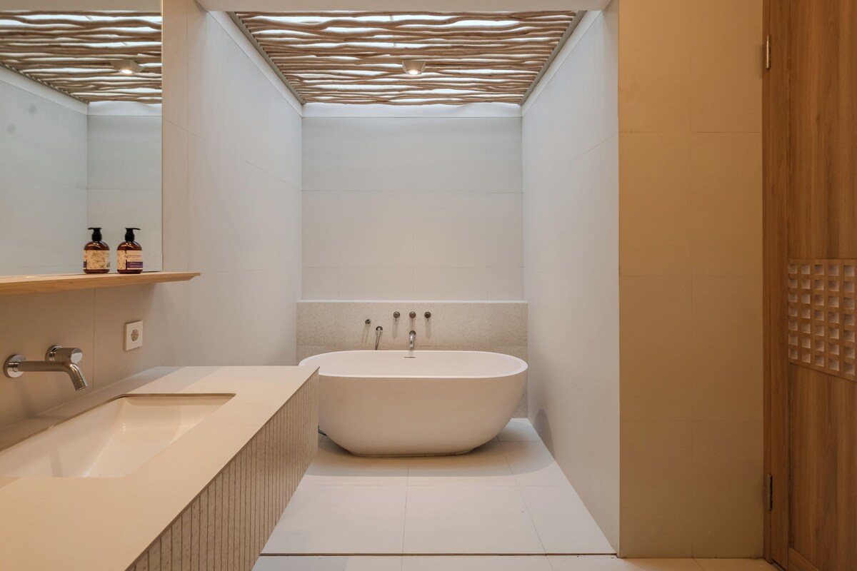 Un baño moderno con una bañera independiente, un tocador con espejo y un estante de madera con artículos de aseo.