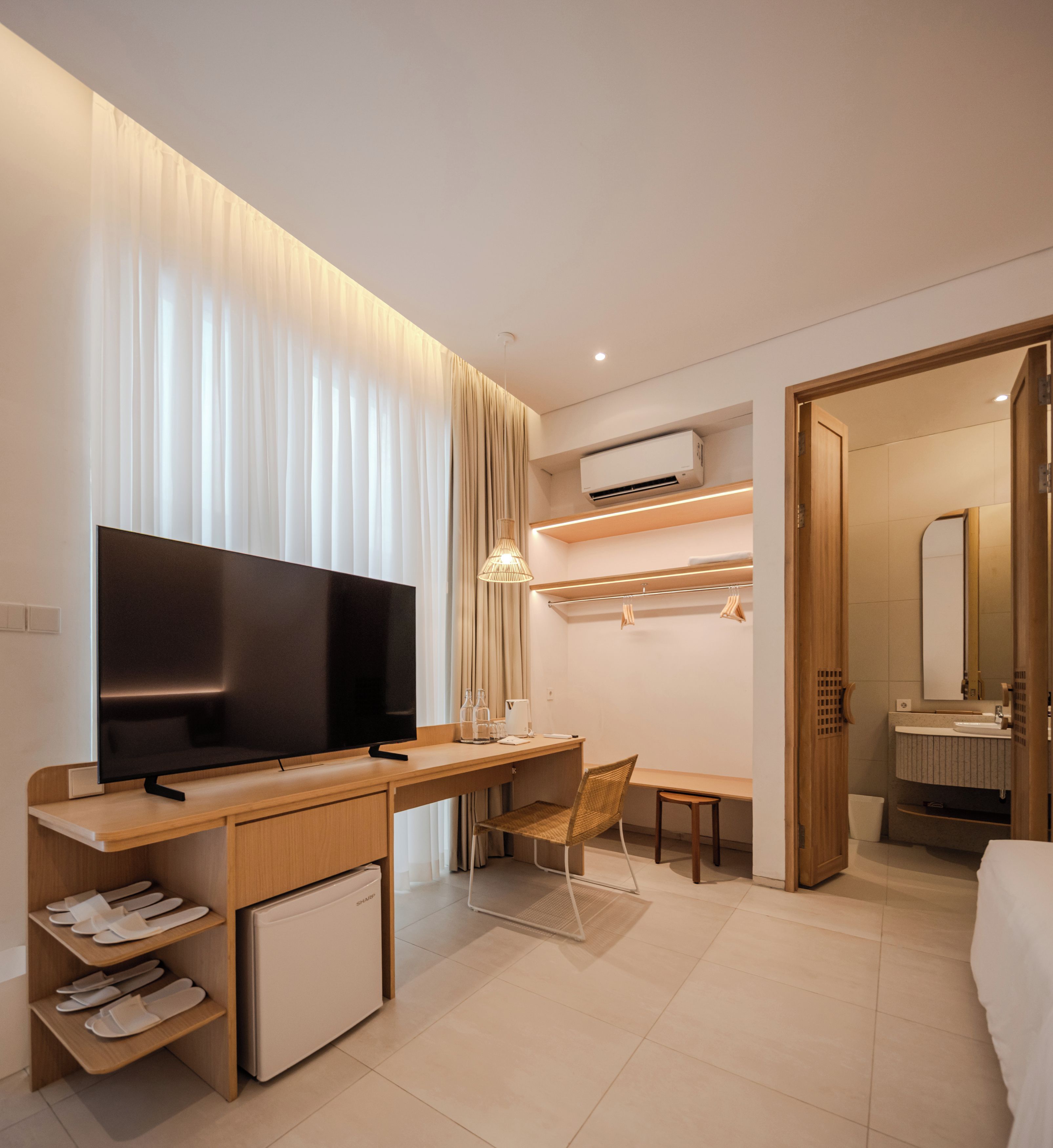 Une chambre d’hôtel moderne équipée d’un téléviseur à écran plat, d’un bureau, d’une chaise, d’un mini-réfrigérateur et d’un système de climatisation intégré.