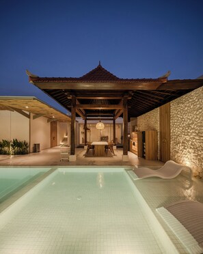 A pool area with a covered seating area and a stone wall. - Astavana Suites Batubelig (Keroboken Kelod)