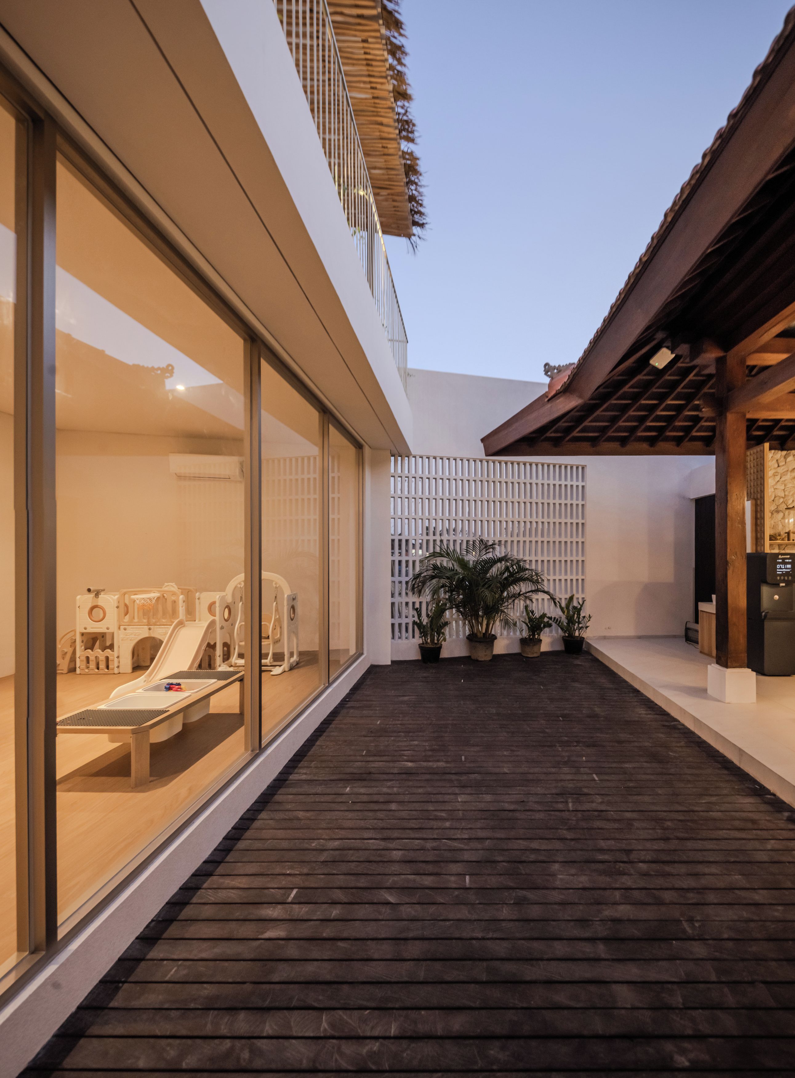 Un espace extérieur moderne doté d’une terrasse en bois, de portes vitrées donnant accès à un espace de jeux et de plantes en pot.