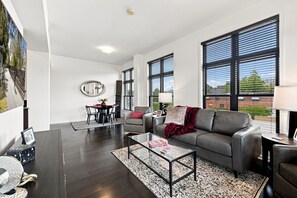 Un salon moderne avec un parquet en bois foncé, une table basse en verre, un canapé gris et un coin repas avec une nappe rouge.