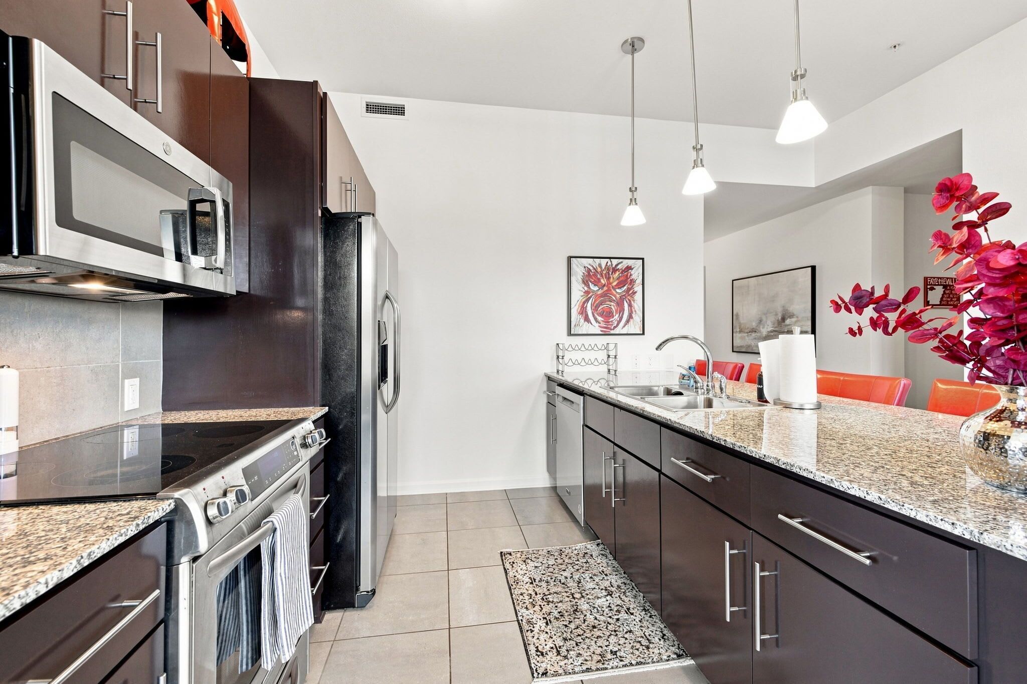 A modern kitchen with stainless steel appliances, a granite countertop, and a dining area with orange chairs.