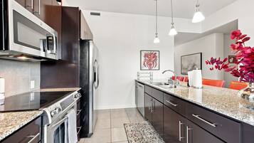 A modern kitchen with stainless steel appliances, a granite countertop, and a dining area with orange chairs.