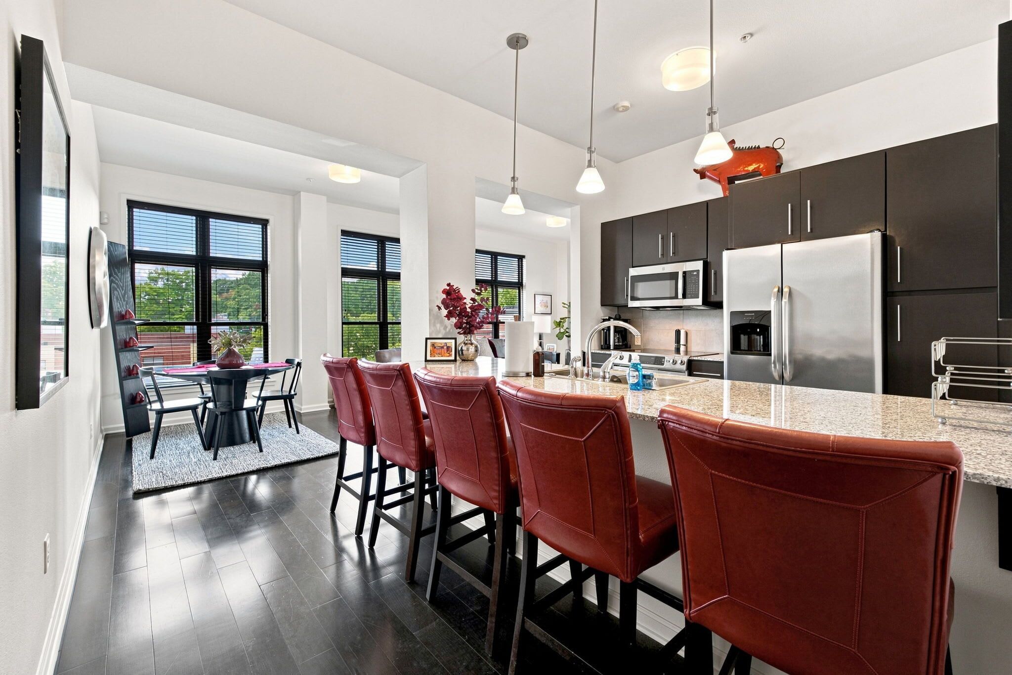 A modern kitchen with dark cabinets, stainless steel appliances, and a bar area with leather chairs.
