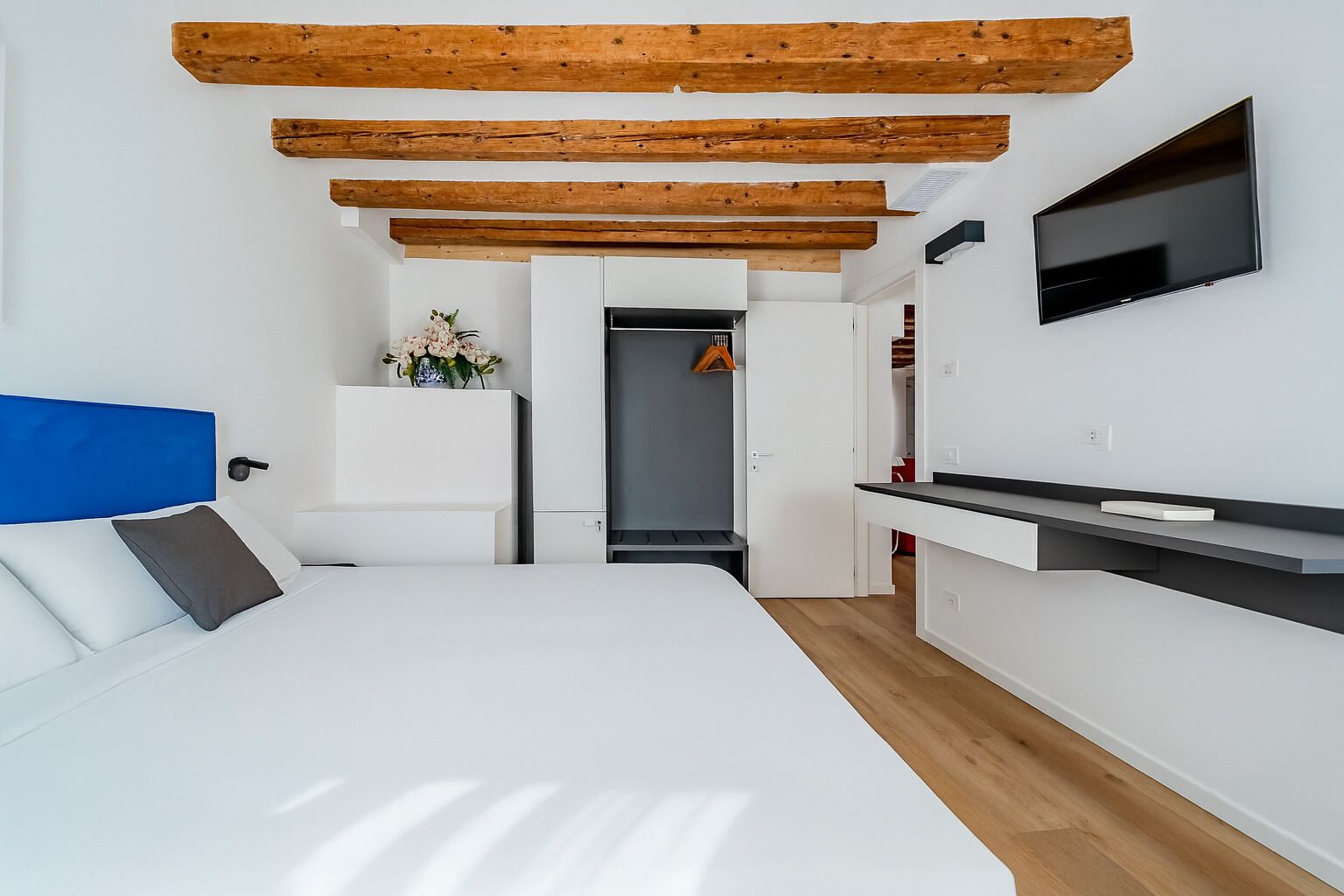 A modern bedroom with a bed, a TV, and a kitchenette.