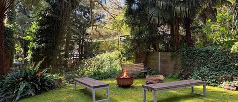 A garden with two benches, a fire pit, and lush greenery.