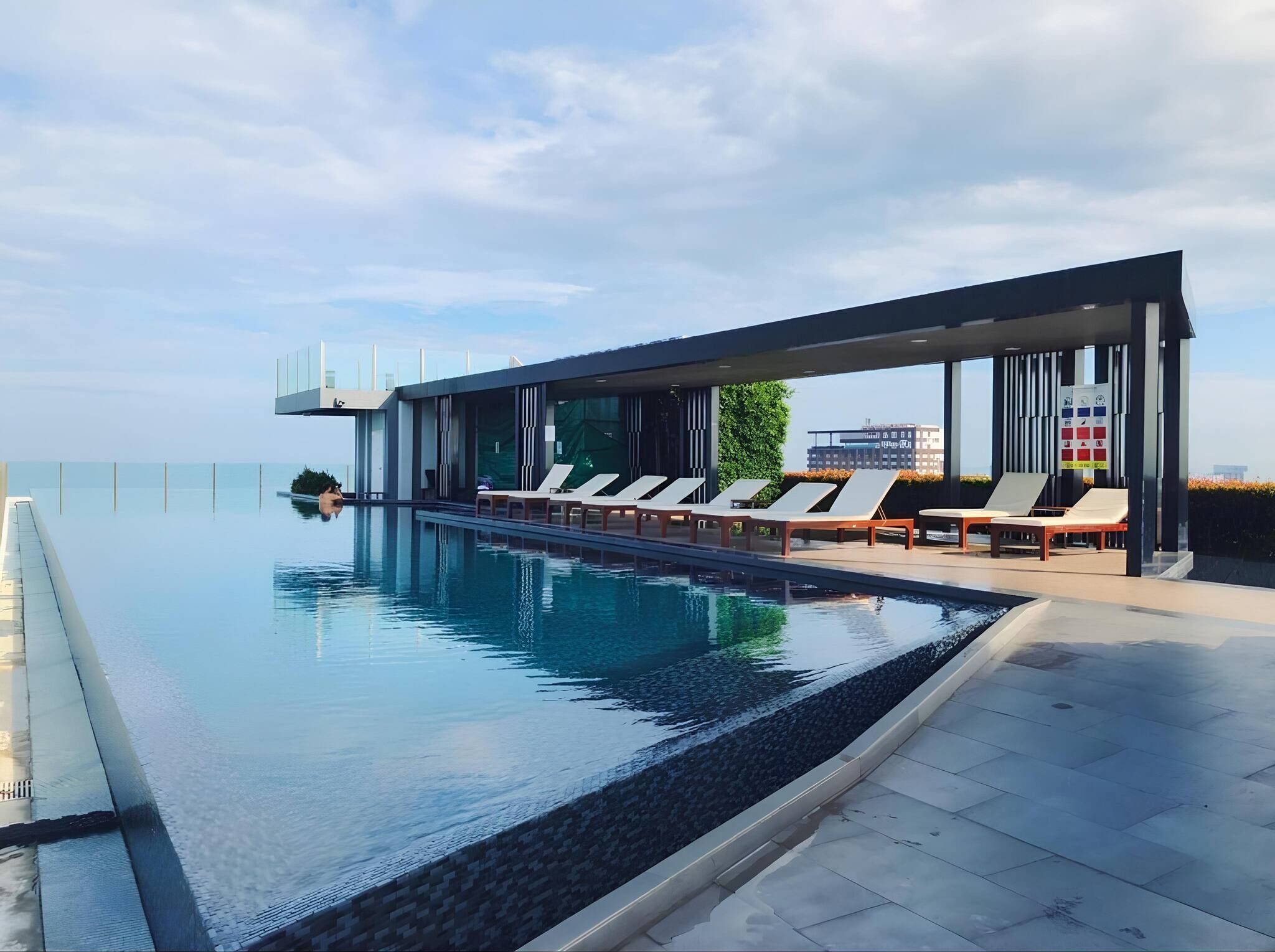 A modern infinity pool with lounge chairs and a covered area, overlooking a cityscape.