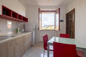 A compact kitchen with a window, a dining table with red chairs, and a view of the outside. - [Appartamento Roberto] 4 beds + A/C (Santo Stefano di Magra)