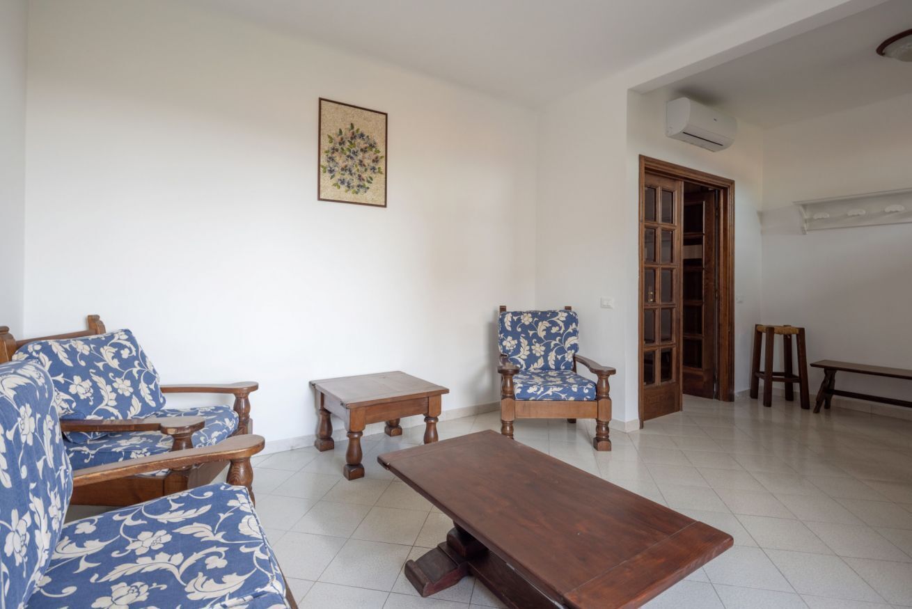 A living room with a sofa, a chair, a coffee table, and a small table. There is a door leading to another room.