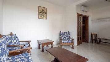 A living room with a sofa, a chair, a coffee table, and a small table. There is a door leading to another room.