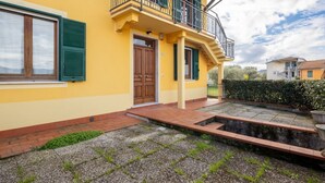 A yellow building with a wooden door, a balcony, and a paved courtyard. - [Appartamento Roberto] 4 beds + A/C (Santo Stefano di Magra)