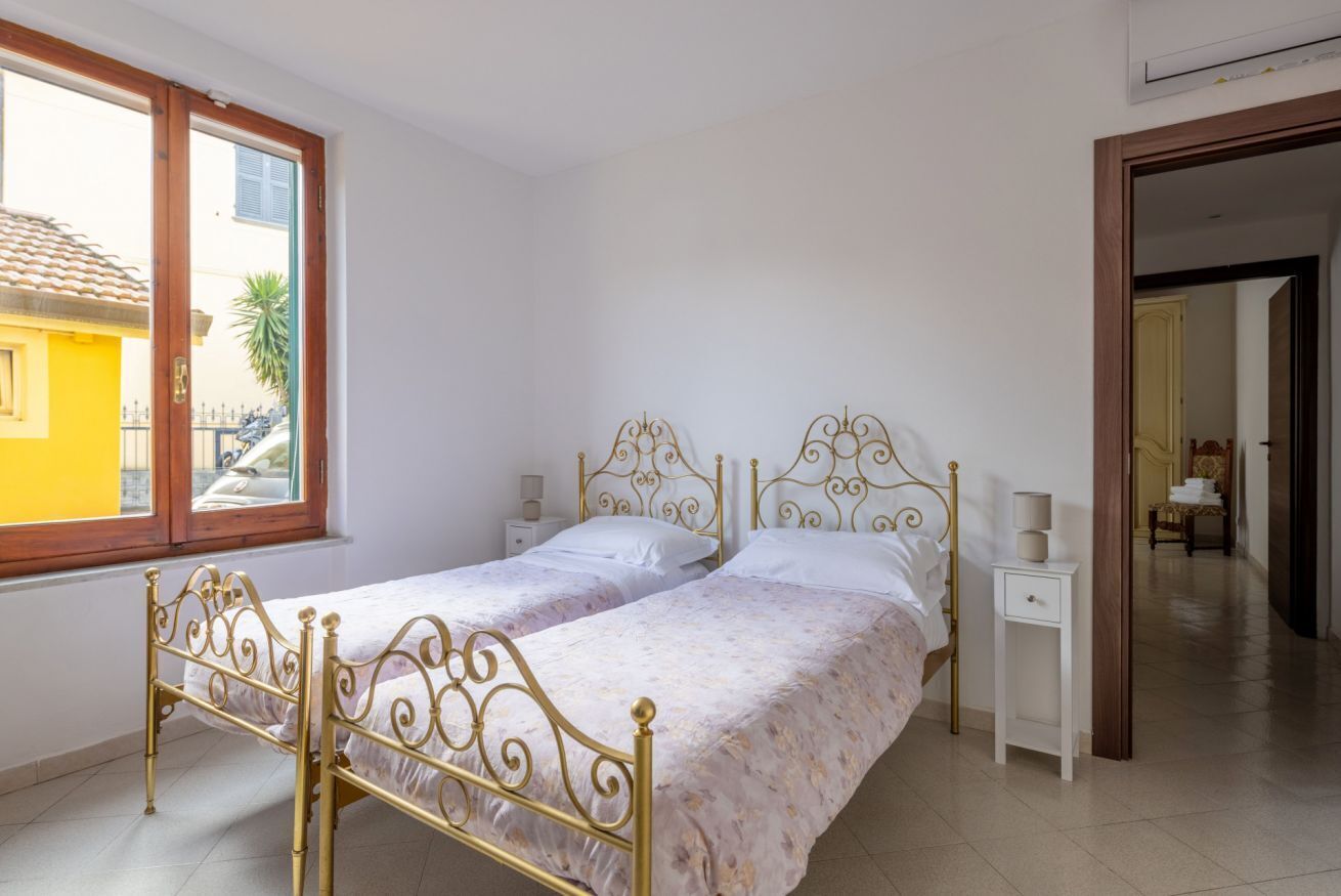 Un dormitorio con cama doble, dos mesitas de noche, una ventana y una puerta que da a otra habitación.