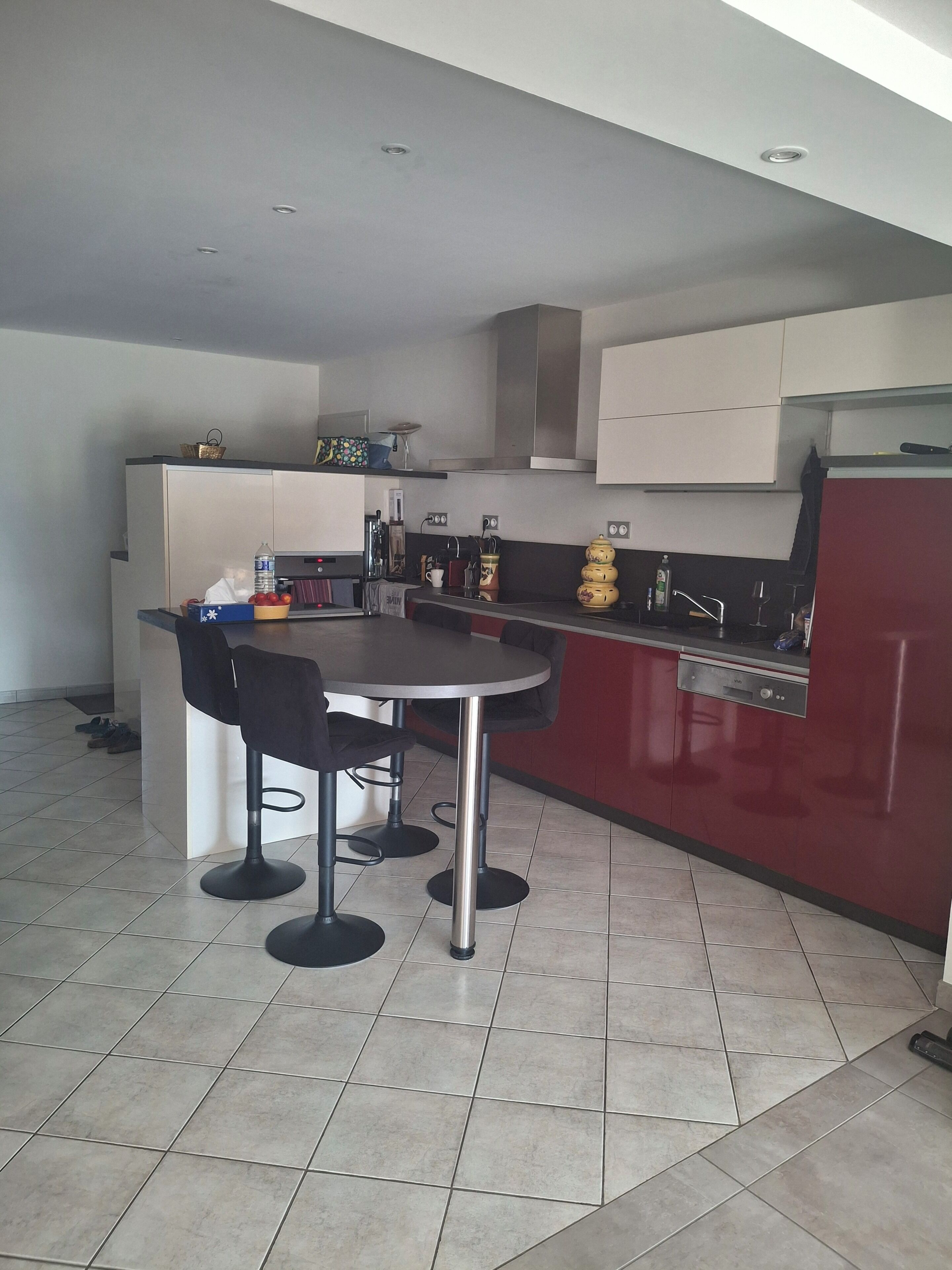 A modern kitchen with a dining area, featuring a round table with four chairs, a red accent wall, and a tiled floor.