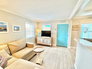 A living room with a sofa, a small round table, a cabinet with a television, and a blue door. - Cozy Cottages, Min 2 Beach, Shops & Restaurants! (San Diego)