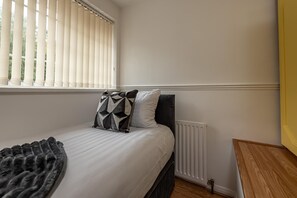 A bedroom with a bed, a radiator, a window with blinds, and a bedside table. - Spacious 3-Bed Home in Wellington | Sleeps 5 - Pass the Keys (Telford)
