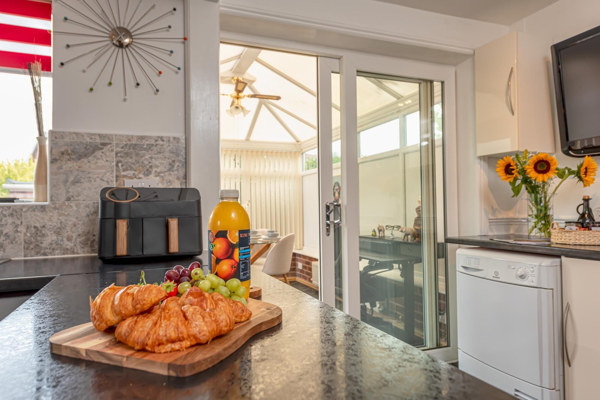 Una cocina con mostrador, un tostador, una botella de jugo de naranja, una tabla de madera con croissants y un lavavajillas.